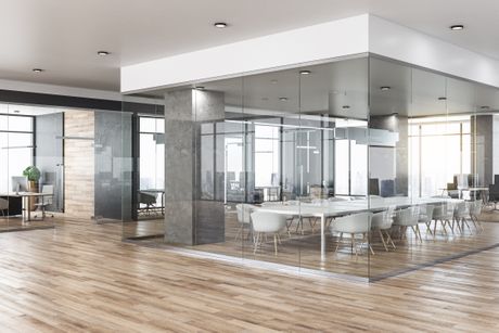 Office space, open plan with light colored wood flooring. Glass encased square office in the center of the floor.